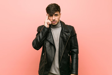 Fototapeta premium Young hispanic man wearing a leather jacket pointing temple with finger, thinking, focused on a task.
