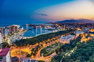 Night aerial panorama of Malaga, Spain with skyscrapers, streets, port, city hall and park during blue hour