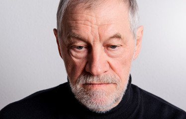 Portrait of a sad senior man with beard and mustache in a studio.