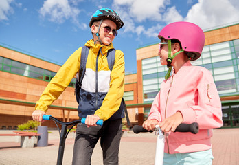Obraz premium education, childhood and people concept - happy school children in helmets with backpacks and scooters outdoors