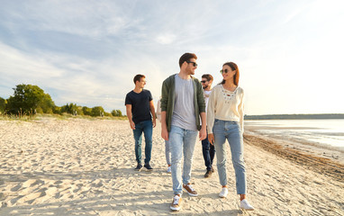 friendship, leisure and people concept - group of happy friends walking along beach in summer