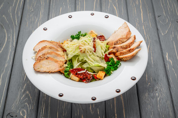 Caesar salad with croutons, quail eggs, cherry tomatoes and grilled chicken on a wooden background