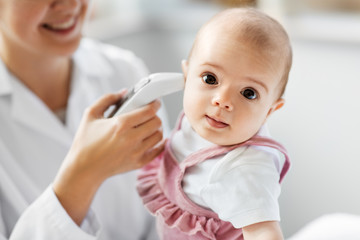 medicine, healthcare and pediatrics concept - female pediatrician doctor with digital infrared thermometer measuring baby girl patient's ear temperature at clinic or hospital