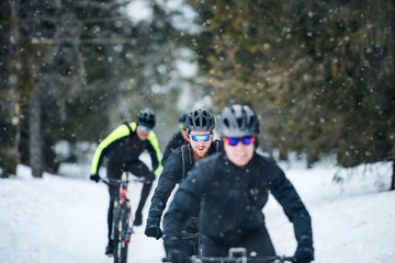 Fototapeta na wymiar Group of mountain bikers riding on road outdoors in winter.