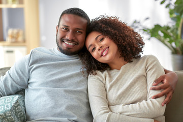 relationships and people concept - happy african american couple sitting on sofa and hugging at home