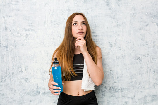 Young caucasian sportswoman holding a isotonic drink looking sideways with doubtful and skeptical expression. - Powered by Adobe