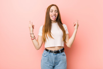 Young redhead ginger woman against a pink wall showing rock gesture with fingers