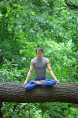 caucasian male meditating in forest  - yoga asana on tree trunk