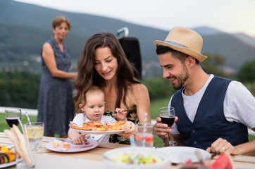 Portrait of family with wine sitting at table outdoors on garden barbecue.