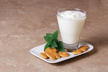 Kefir in a glass goblet with a mint branch with cookies on a wooden board on a brown background