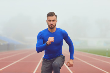 Obraz premium The guy the athlete does squats in the stadium in the fog