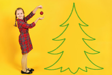 Happy little girl decorates a Christmas tree. A child in a full-length in the red dress on a yellow background