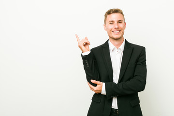 Young caucasian business man smiling cheerfully pointing with forefinger away.