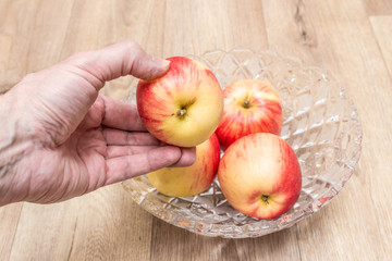 Hand puts apples in a glass plate