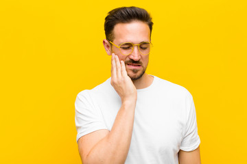 young handsome man holding cheek and suffering painful toothache, feeling ill, miserable and...