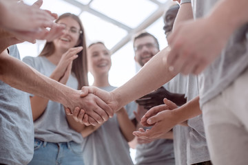 handshake of young people on the background of the applauding team - obrazy, fototapety, plakaty