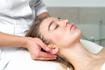 Obraz premium Young caucasian woman lying down receiving a head massage by female beautician touching woman's ears and temples in the spa beauty salon close up.