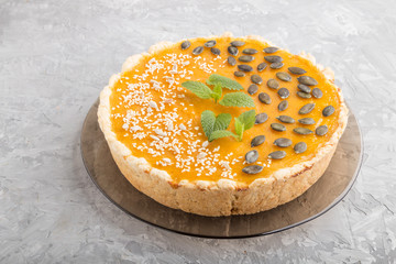 Traditional american sweet pumpkin pie decorated with mint, sesame and pumpkin seeds on a gray concrete background. side view.
