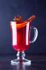 Red hot mulled wine with spices on dark background. Christmas mulled wine with orange, star anise and cinnamon. One glass of mulled wine and copy space