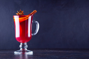 Red hot mulled wine with spices on dark background. Christmas mulled wine with orange, star anise and cinnamon. One glass of mulled wine and copy space