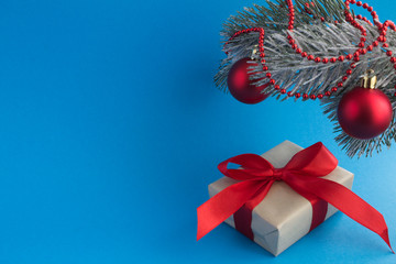 Christmas composition: gift with red bow and spruce branch on the blue background. Copy space.