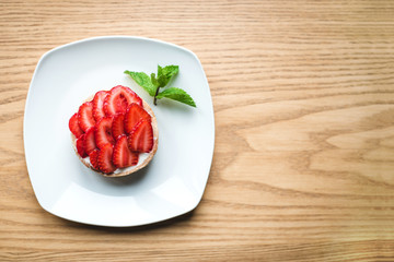 Strawberry tartlet on wooden table near the window.