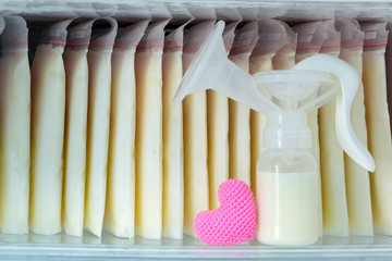 Stock of breast milk frozen in storage bags and a pump bottle for a new baby of family and pink...
