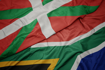 waving colorful flag of south africa and national flag of basque country.