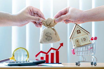 Businessman hand hold a money bag and home and red bar graph with growing value  in the office, agreement as business investment for real estate or loan contract for buy a house concept.