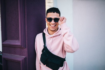 Obraz premium City portrait of handsome hipster guy wearing pink blank hoodie with black waist bag with space for your logo or design. Mockup for print