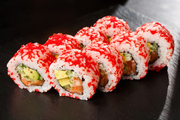 Sushi Rolls with avocado, cucumber and salmon inside on black slate isolated. California rolls covered orange tobiko or masago caviar. Sushi menu. Horizontal photo.