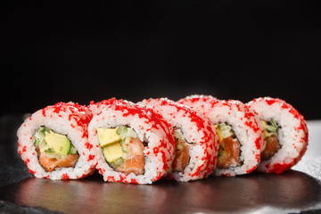 Sushi Rolls with avocado, cucumber and salmon inside on black slate isolated. California rolls covered orange tobiko or masago caviar. Sushi menu. Horizontal photo.