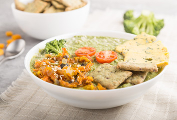 Green broccoli cream soup with crackers in white bowl on a gray concrete background, side view, selective focus.