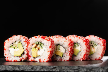 Sushi Rolls with avocado, eel, cucumber and cream cheese inside on black slate isolated. California rolls covered orange tobiko or masago caviar. Sushi menu. Horizontal photo.