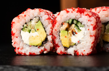 Sushi Rolls with avocado, eel, cucumber and cream cheese inside on black slate isolated. California rolls covered orange tobiko or masago caviar. Sushi menu. Horizontal photo.