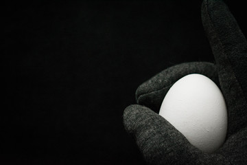 White egg in a hand on a black background