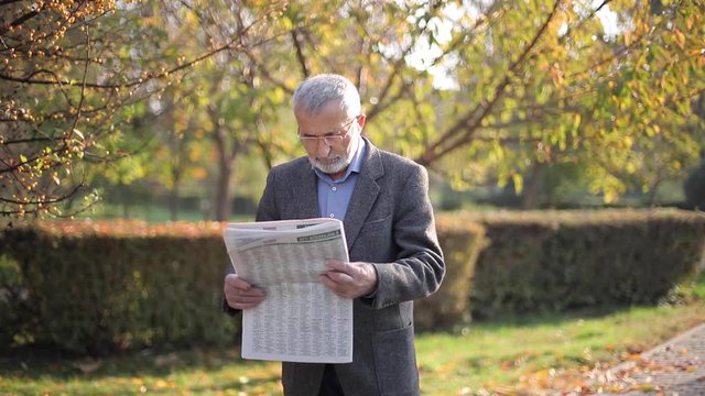 Senior man read a newspaper in the park. Background of yellow tree in autumn