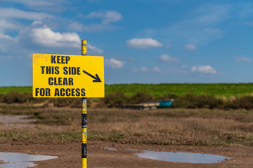 Sign: Keep This Side Clear For Access, seen in Burnham Overy Staithe, Norfolk, England, UK - with a boat in the Overy Marshes in the background