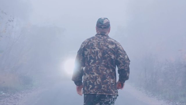Aggressive man with an ax is walking in the fog towards the car