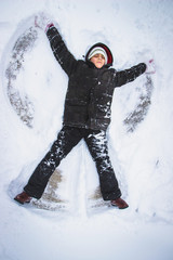 Fototapeta na wymiar Cute boy playing outside, making star in snow. Winter time, winter activity