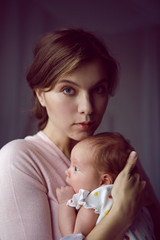 mother in a white robe holds a small newborn daughter against the wall