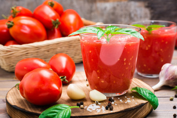 Fresh tomato juice with basil leaves in glasses and ingredients for its preparation on a wooden table