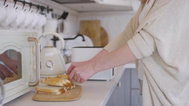 Dolly-in shot with mid-section of unrecognizable woman putting slices of bread into toaster