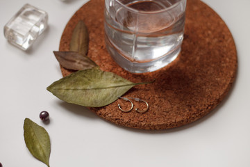 earrings women's jewelry lie on a green leaf close up on a stand cork and a glass of water on a light background
