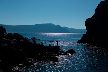 Tourists on the rocks and boats near Amoudi Bay on Santorini Island in Greece.