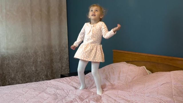 Little girl jumping on the bed. A child in a skirt smiles and laughs. Slow motion