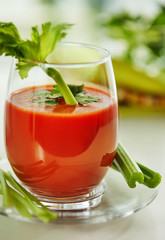 Tomato juice on a white plate with a garnish of celery and parsley. Healthy eating concept.