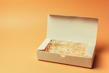 Open gift white box inside with paper hay on a beige background, isolate. Copyspace. The concept of sales, discounts, Christmas gifts and shopping.