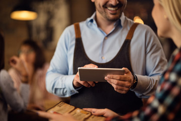Close-up of waiter using digital tablet while serving a guest in a pub.