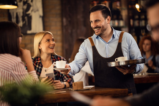 Happy Waiter Serving Coffee To Young Women In A Cafe.